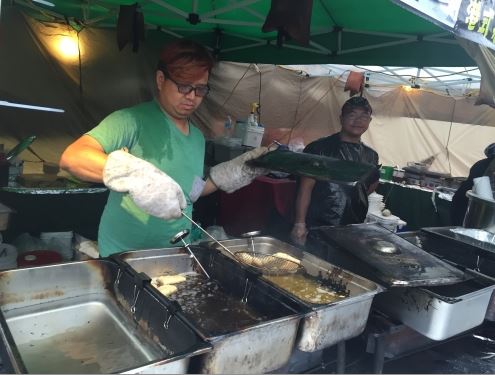 A man is preparing food at an outdoor market.
