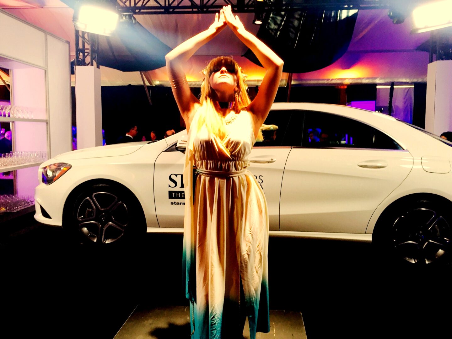 A woman in a long dress standing in front of a white car.